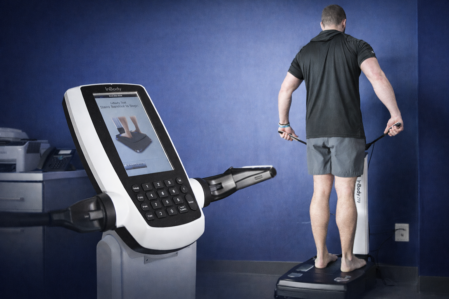 Person standing on the InBody Scale beside an image of the InBody screen